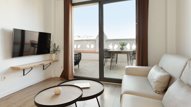 Un salon moderne comprenant un canapé, deux petites tables, un téléviseur et une porte-fenêtre coulissante donnant sur un balcon extérieur.