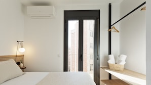 Une chambre d’hôtel équipée d’un lit, d’une lampe de chevet, d’un appareil de climatisation, d’une fenêtre et d’une étagère avec des serviettes.