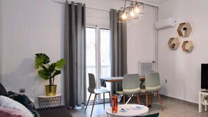 A modern living room with a sofa, a dining table with chairs, a potted plant, and a TV stand. - New Apartment in the heart of Koukaki Orlof str (Athens)