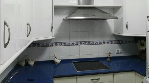 Una cocina con armarios blancos, encimera azul y campana extractora de acero inoxidable.