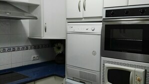 Una cocina compacta con armarios blancos, horno empotrado, microondas y lavadora.