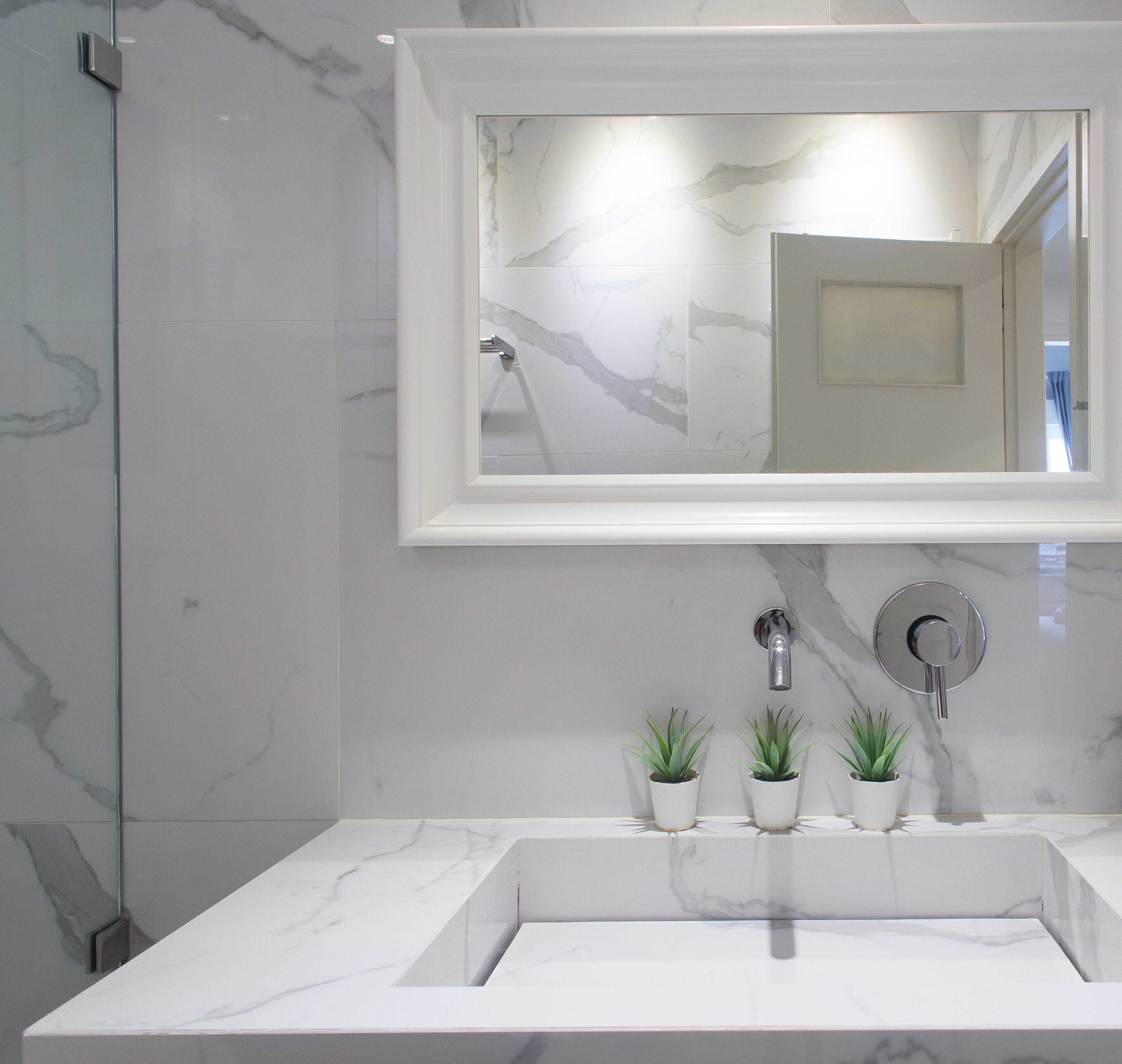 A bathroom with a white marble sink, a mirror, and two potted plants.