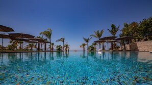 A clear blue pool with tiled mosaic patterns, surrounded by palm trees and umbrellas. - El Primero Hotel (Sarandë)