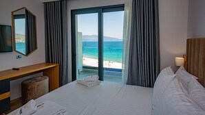 A hotel room with a bed, a desk, a TV, and a view of the beach. - El Primero Hotel (Sarandë)