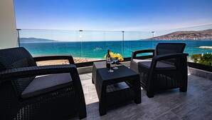 A balcony with wicker furniture, a glass table, and a view of the sea and distant hills. - El Primero Hotel (Sarandë)
