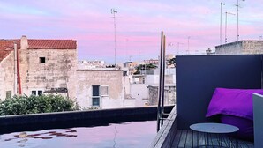 Terraza en la azotea con piscina, una pequeña mesa y un cojín morado.