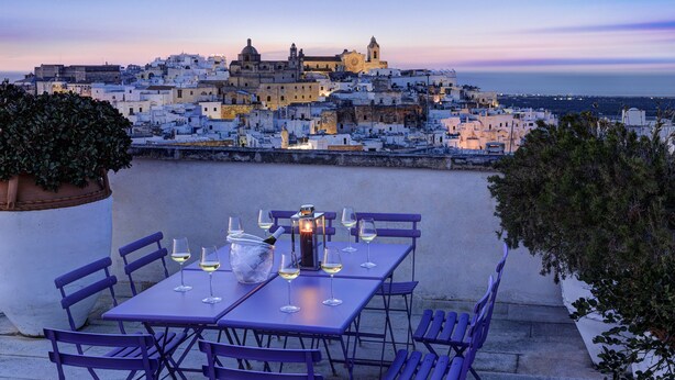 Terraza en la azotea con una mesa preparada para comer, con vistas a un paisaje urbano al atardecer.