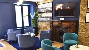 Una habitación con chimenea, sillones azules, un televisor y un ventanal grande.