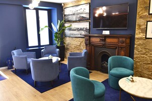 Una habitación con chimenea, sillones azules, un televisor y un ventanal grande.