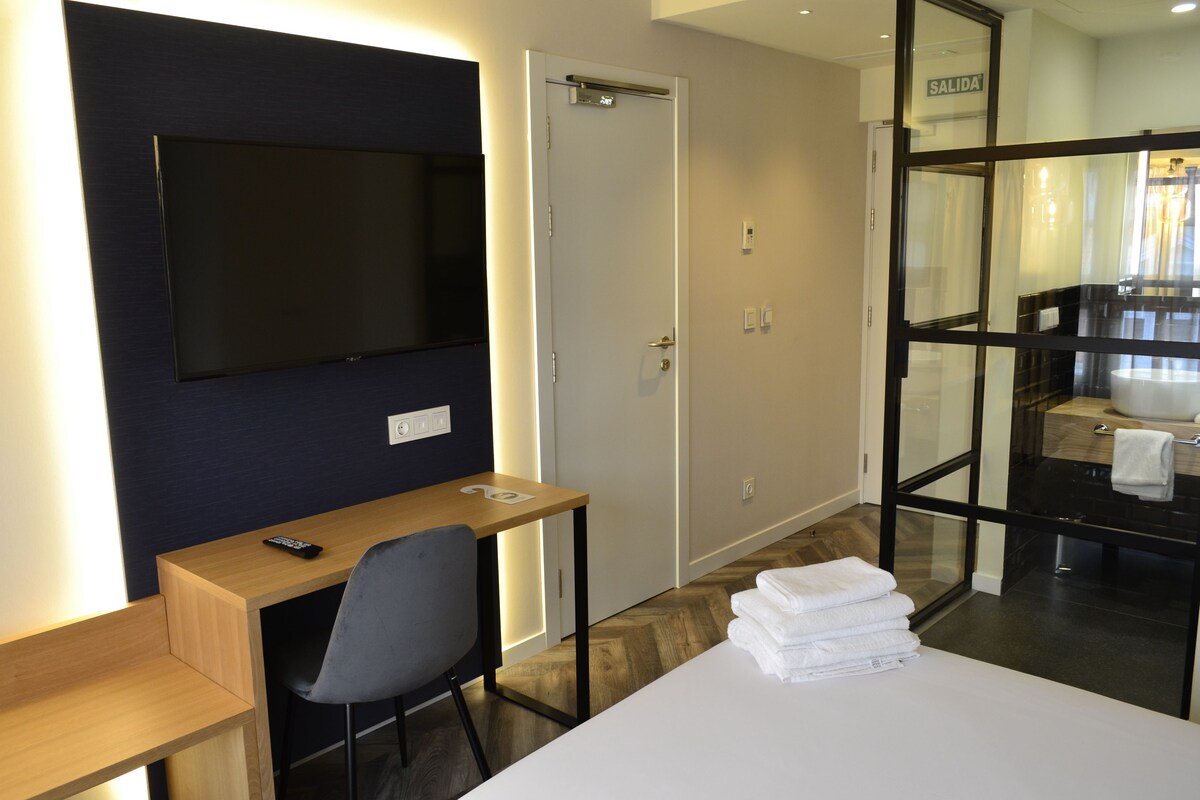 Habitación de hotel con televisión, escritorio, silla y cama con toallas dobladas con cuidado.