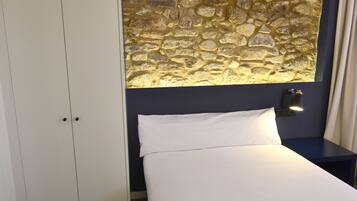 A hotel room with a bed, a nightstand, a wall-mounted lamp, and a wardrobe.