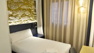 A hotel room with a bed, a desk, a lamp, and a window with curtains.