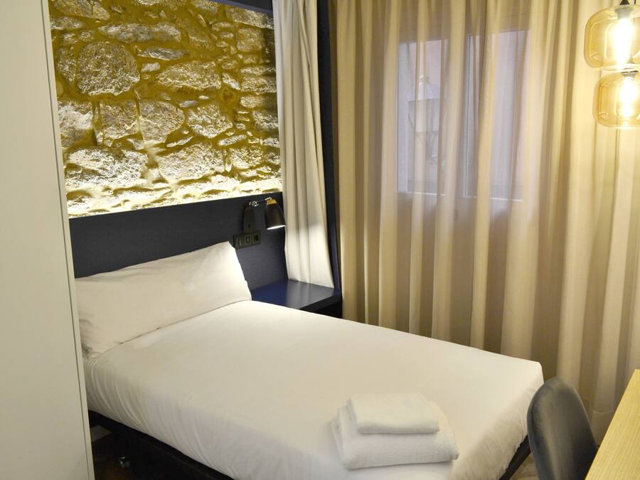A hotel room with a bed, a desk, a lamp, and a window with curtains.