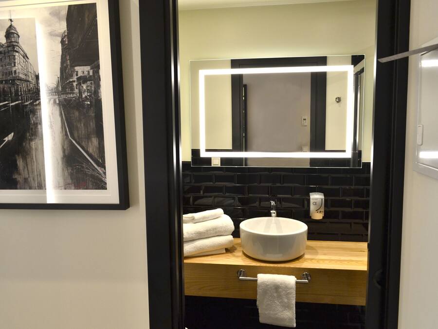 Une salle de bain moderne avec un mur recouvert de carreaux noirs, un lavabo rond et une photographie en noir et blanc encadrée accrochée au mur.