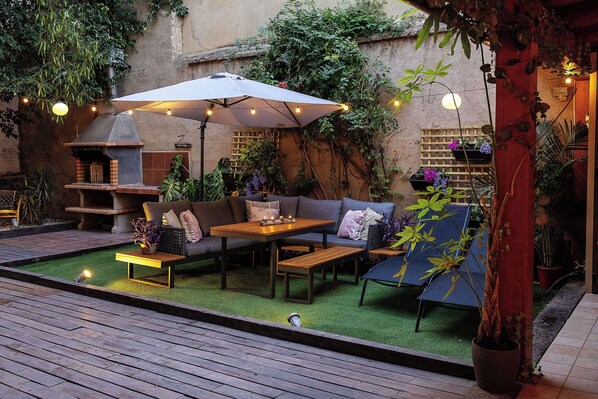 Un patio con una parrilla, muebles de exterior y plantas en macetas.