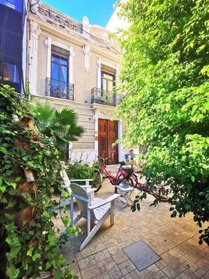 Un patio con un edificio que tiene una puerta de madera y un balcón con barandilla de hierro forjado.