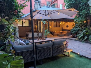 Un patio al aire libre con mobiliario de mimbre, una zona de estar cubierta y césped artificial.