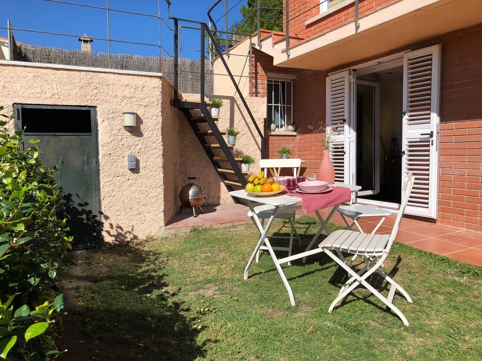 Un pequeño patio con una mesa lista para dos personas, una parrilla y un jardín.
