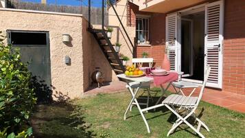 Un pequeño patio con una mesa lista para dos personas, una parrilla y un jardín.