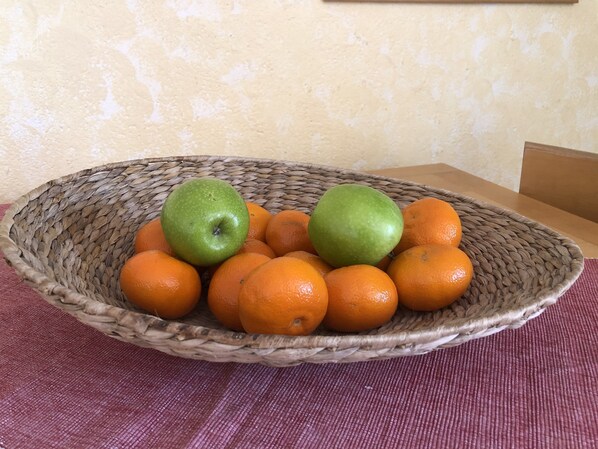 A woven basket containing oranges and green apples on a table.