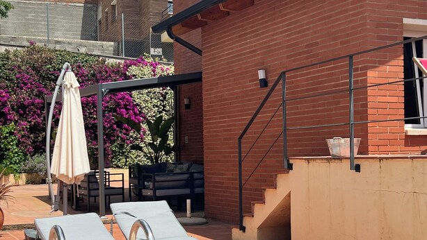 A swimming pool with two lounge chairs and a sun umbrella, surrounded by a brick wall and a garden with purple flowers. - Beautiful apartment, garden and swimming pool, 20km from Barcelona, suitable for pets (Vallirana)
