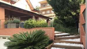 A staircase with white pebbles leading up to a wooden deck, surrounded by greenery and a brick wall. - Beautiful apartment, garden and swimming pool, 20km from Barcelona, suitable for pets (Vallirana)