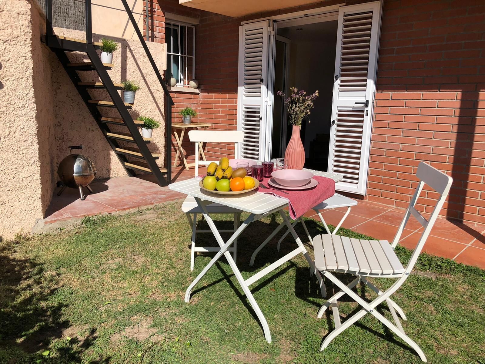 A patio with a table set for two, a grill, and potted plants.
