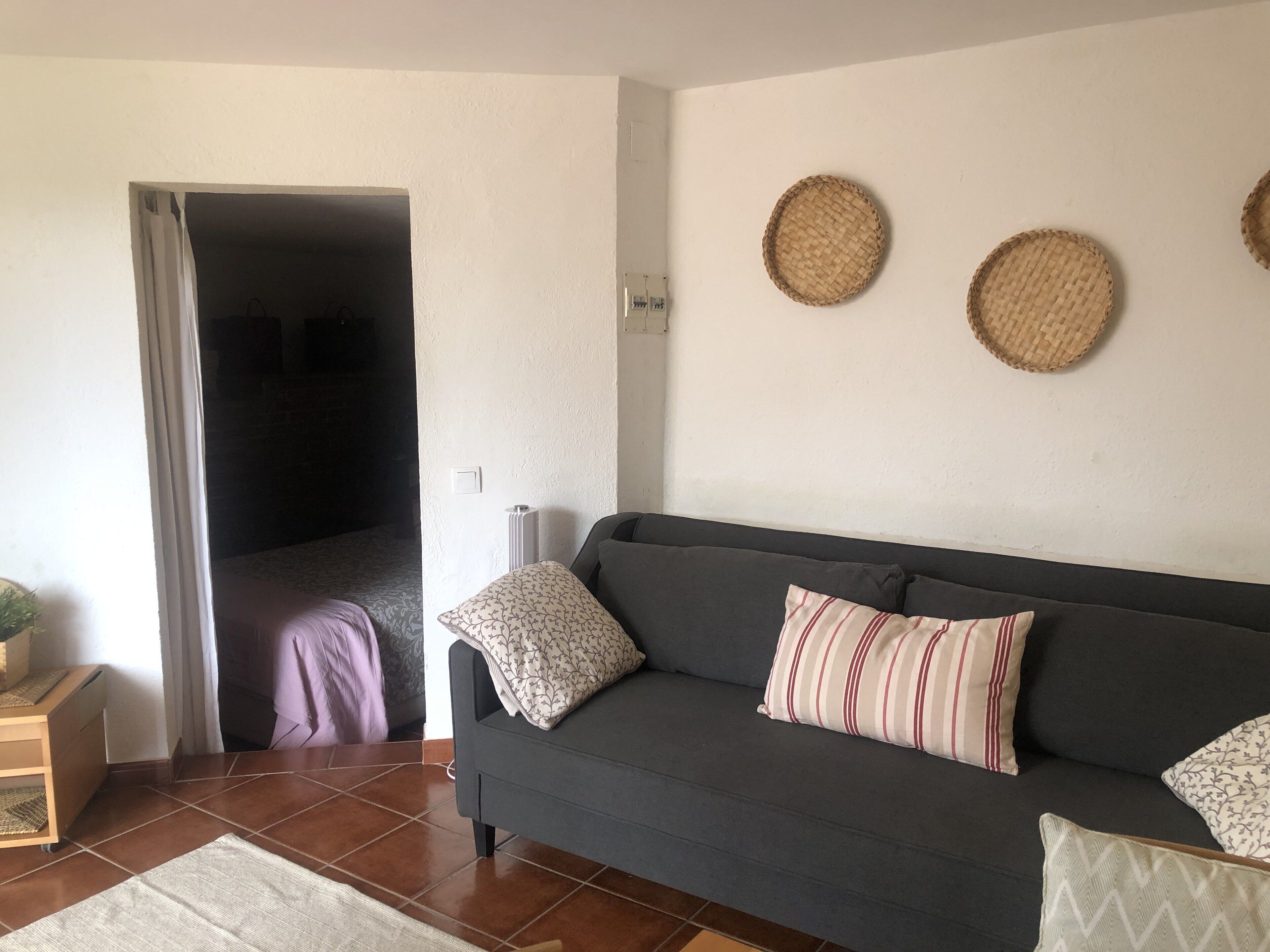 Un salon avec un canapé gris foncé, des coussins à motifs, une petite table d’appoint en bois et une décoration murale tissée.