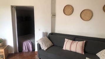 Un salon avec un canapé gris foncé, des coussins à motifs, une petite table d’appoint en bois et une décoration murale tissée.