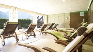 A sunlit room with wooden lounge chairs and a view of mountains through large windows. - Hotel Birkenhöhe (Mittelberg)