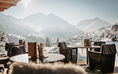 A cozy outdoor seating area with wicker chairs and tables, overlooking a snowy mountain landscape.