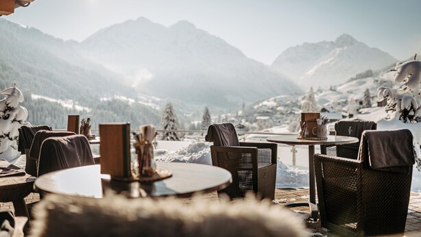 A cozy outdoor seating area with wicker chairs and tables, overlooking a snowy mountain landscape. - Hotel Birkenhöhe (Mittelberg)