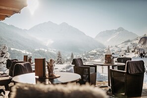 A cozy outdoor seating area with wicker chairs and tables, overlooking a snowy mountain landscape. - Hotel Birkenhöhe (Mittelberg)