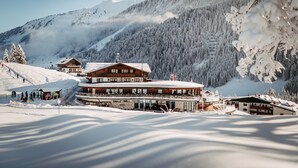 A large wooden lodge with multiple floors, surrounded by snow-covered mountains and trees. - Hotel Birkenhöhe (Mittelberg)
