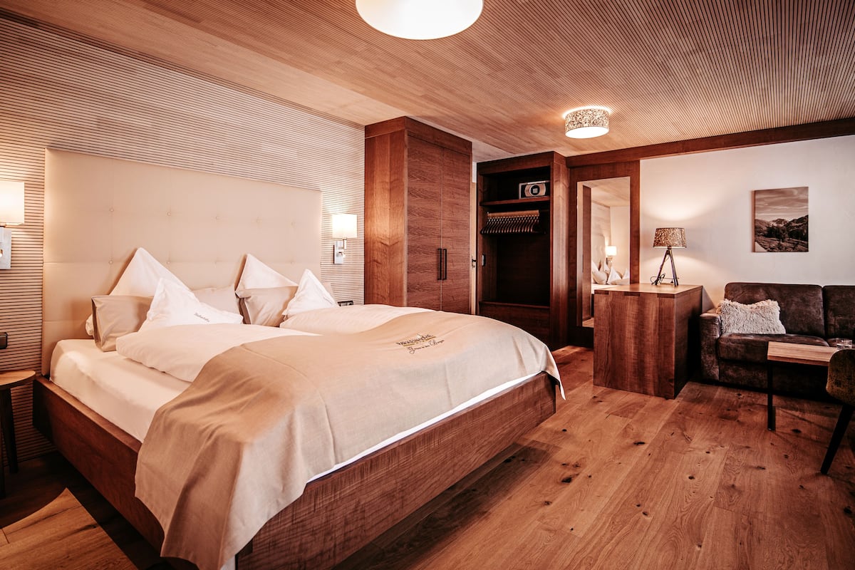 A wooden-floored bedroom with a large bed, a wooden wardrobe, a desk, and a chair.