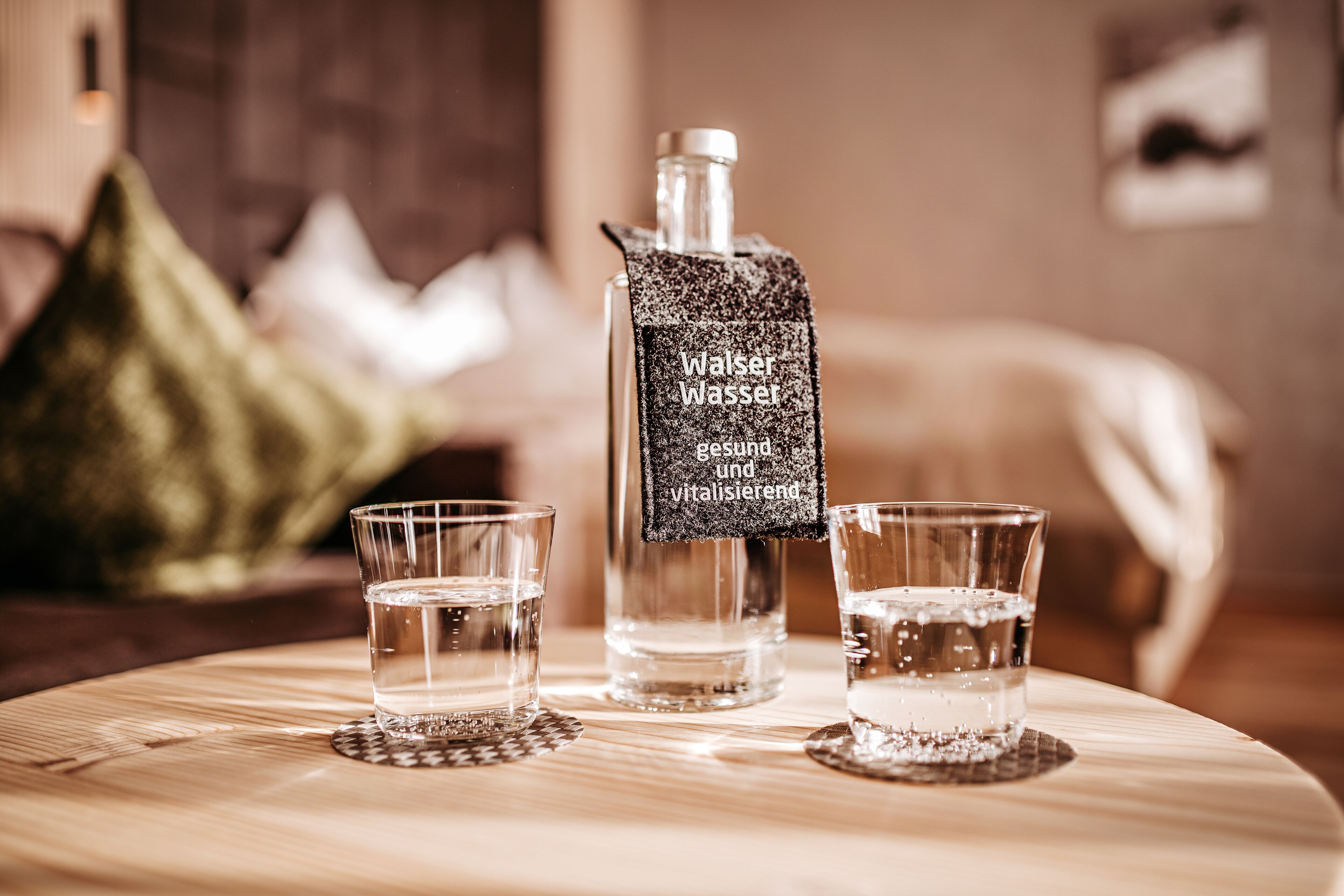 A bottle of water with a label on a wooden table, accompanied by two glasses of water.