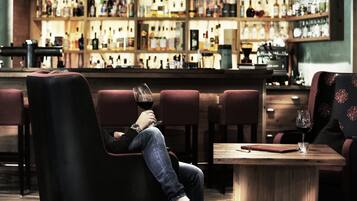 Un'area bar con un bancone in legno e scaffali pieni di bottiglie. Diverse poltrone imbottite e un tavolo con un bicchiere di vino.