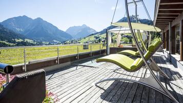 A wooden deck with green lounge chairs and a view of mountains.
