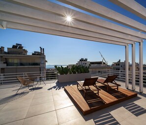 Une terrasse sur le toit, dotée de chaises longues, d’un sol carrelé et offrant une vue sur le paysage urbain.