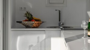 Een moderne keuken met een wit aanrecht, een schaal met fruit, een wijnglas en een klein raam.
