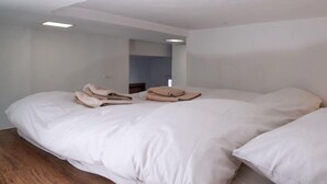 Une chambre avec un grand lit, un plancher en bois et un miroir au mur.