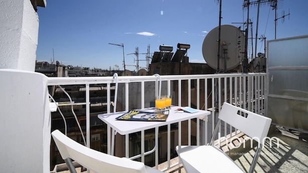 Un balcon avec des chaises blanches et une table, un magazine et un verre de jus d’orange.
