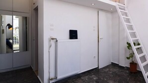 Un intérieur moderne avec un radiateur blanc, un objet noir accroché au mur, une échelle blanche et une plante en pot.