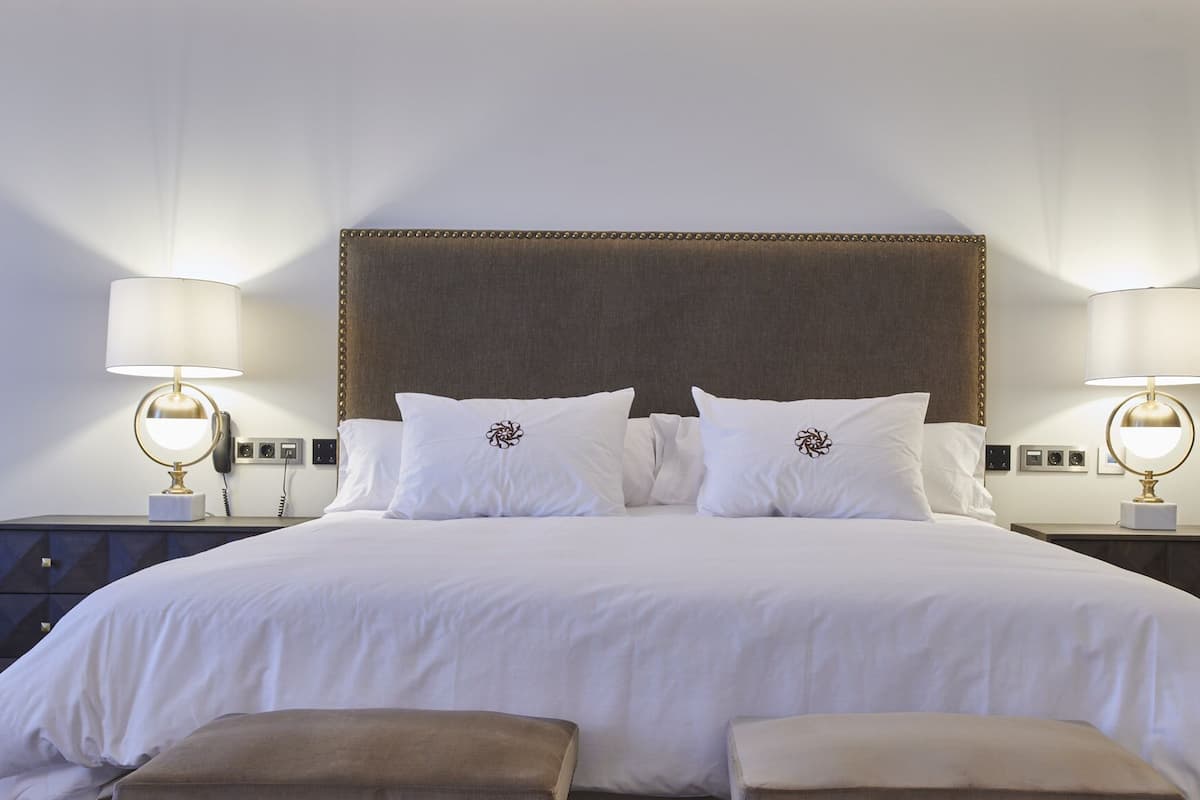 A neatly made bed with white linens and decorative pillows, flanked by two bedside tables with lamps, in a modern hotel room.