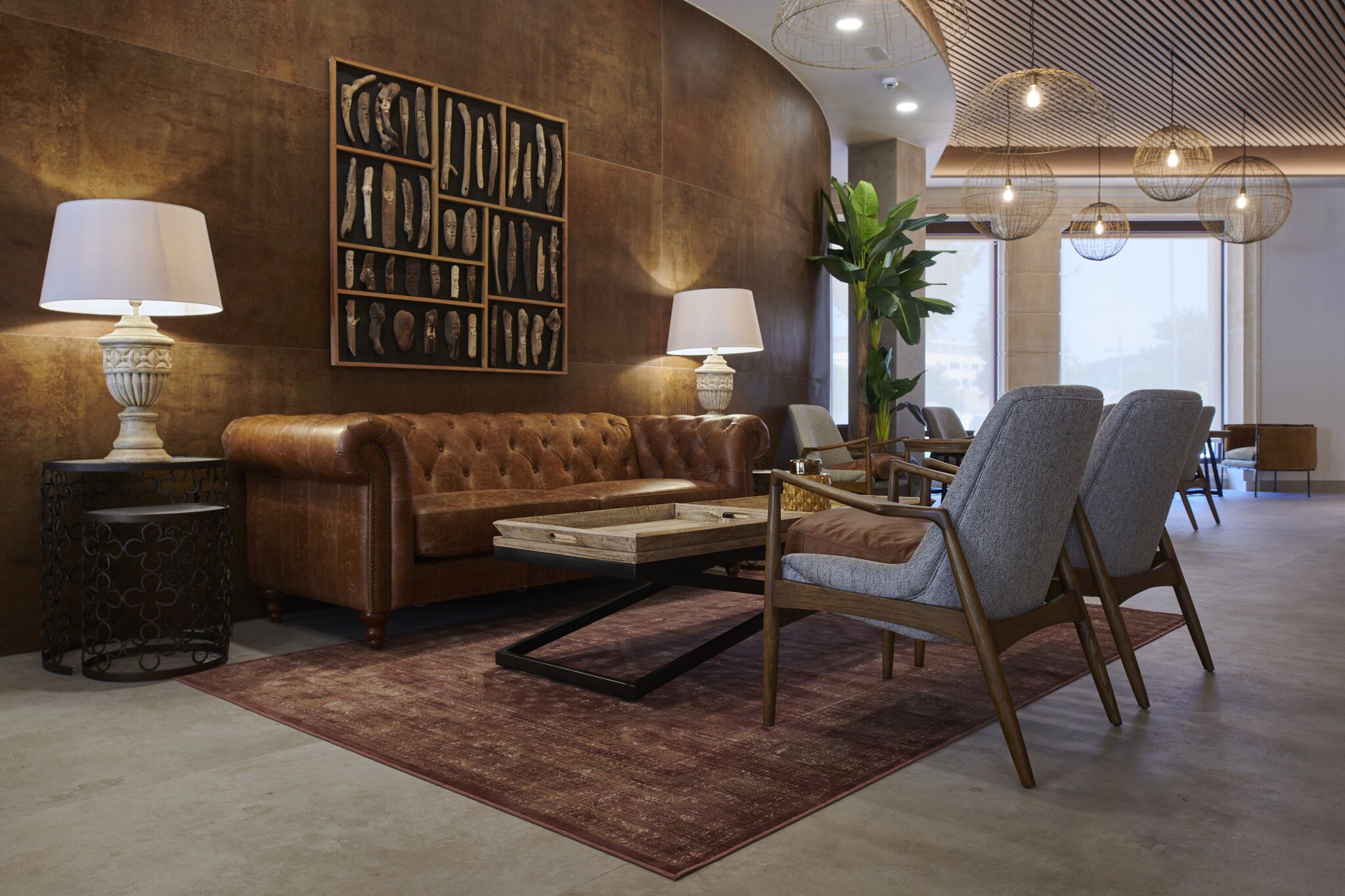 Un hall d’entrée moderne avec un canapé en cuir marron, deux fauteuils, une table basse et une œuvre d’art accrochée au mur.