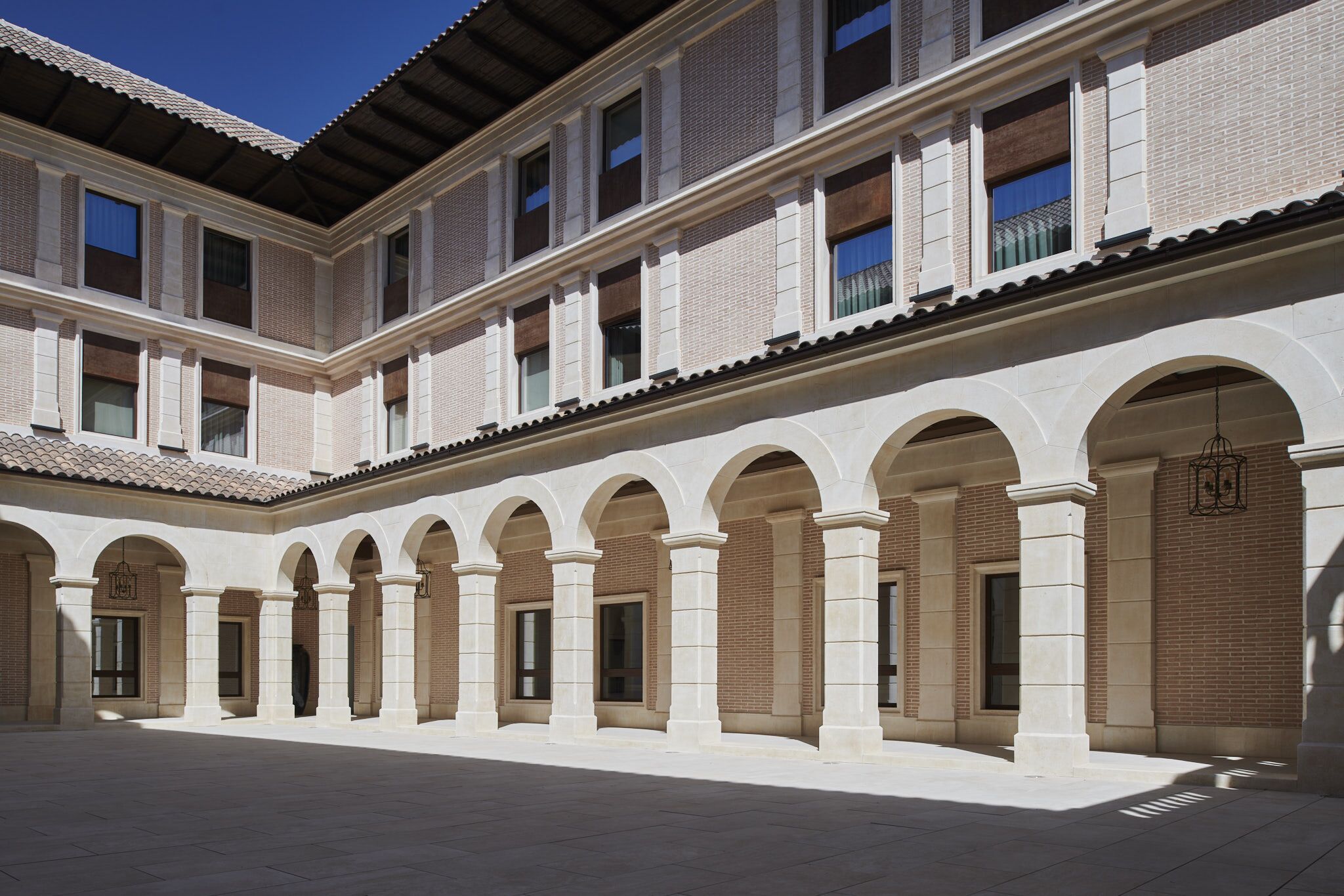 Un cortile con una serie di archi e colonne, un tetto in tegole e una facciata in mattoni.
