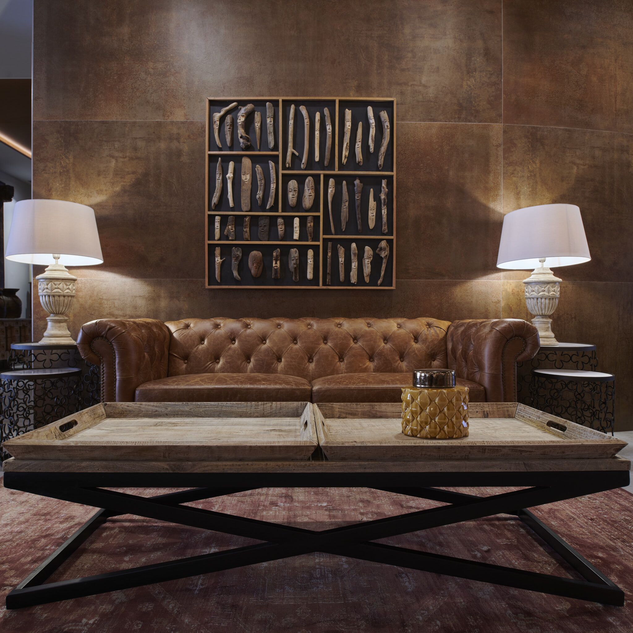 A brown leather sofa with a wooden tray in front, flanked by two side tables with lamps.