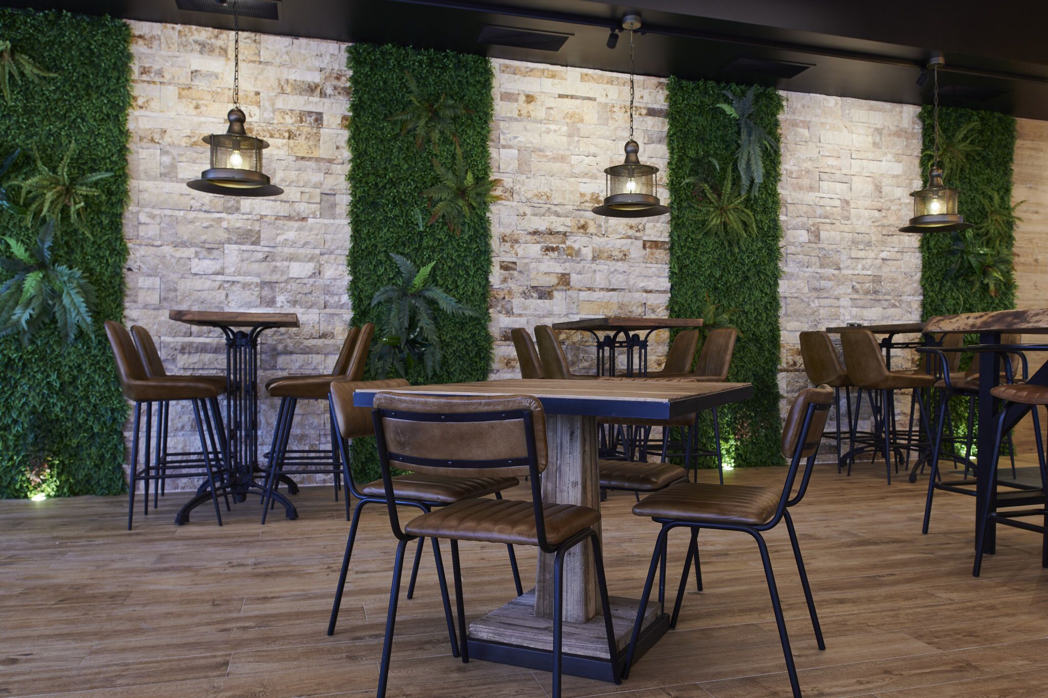 Interior de un restaurante con paredes de ladrillo, follaje verde y muebles de madera.