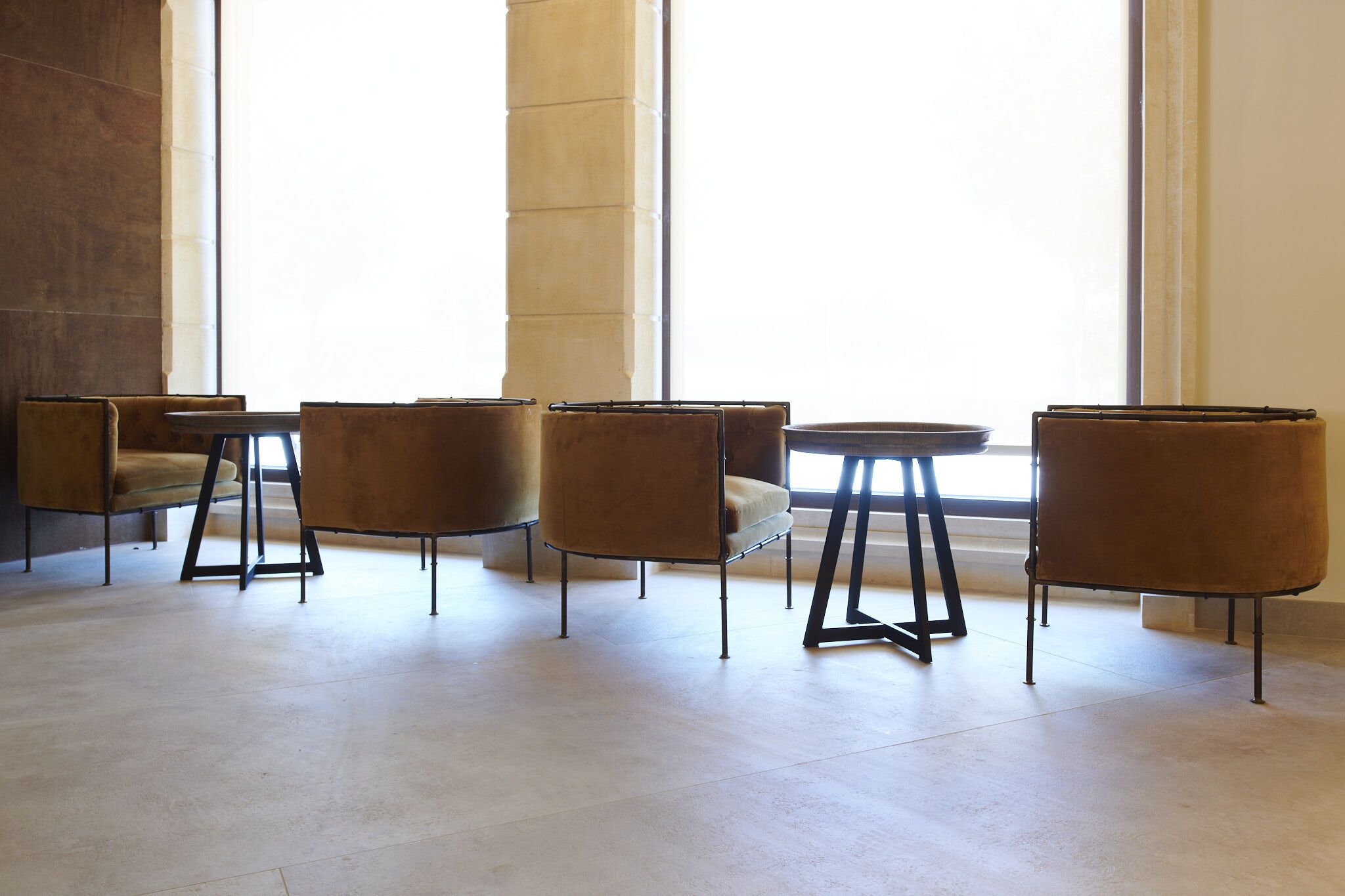 Un intérieur moderne avec quatre chaises marron à coussins et une petite table ronde, disposées en rangée devant une grande fenêtre.