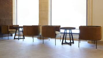 A modern interior with four brown cushioned chairs and a small round table, arranged in a row with a large window in the background.